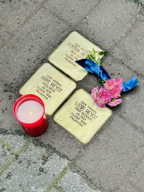 Drei Stolpersteine im Boden mit Kerze und Blumen