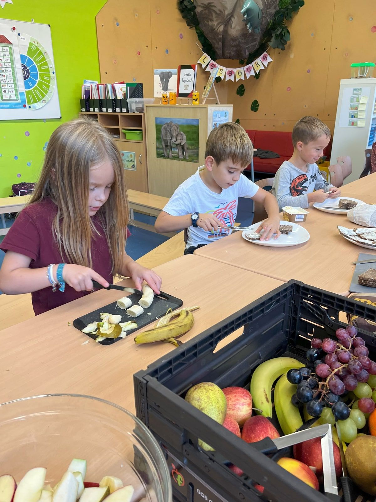 Drei Kinder schneiden Obst und schmieren Brot