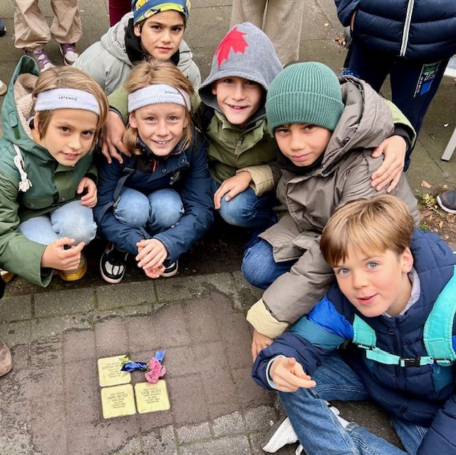 Kinder hocken um drei Stolpersteine