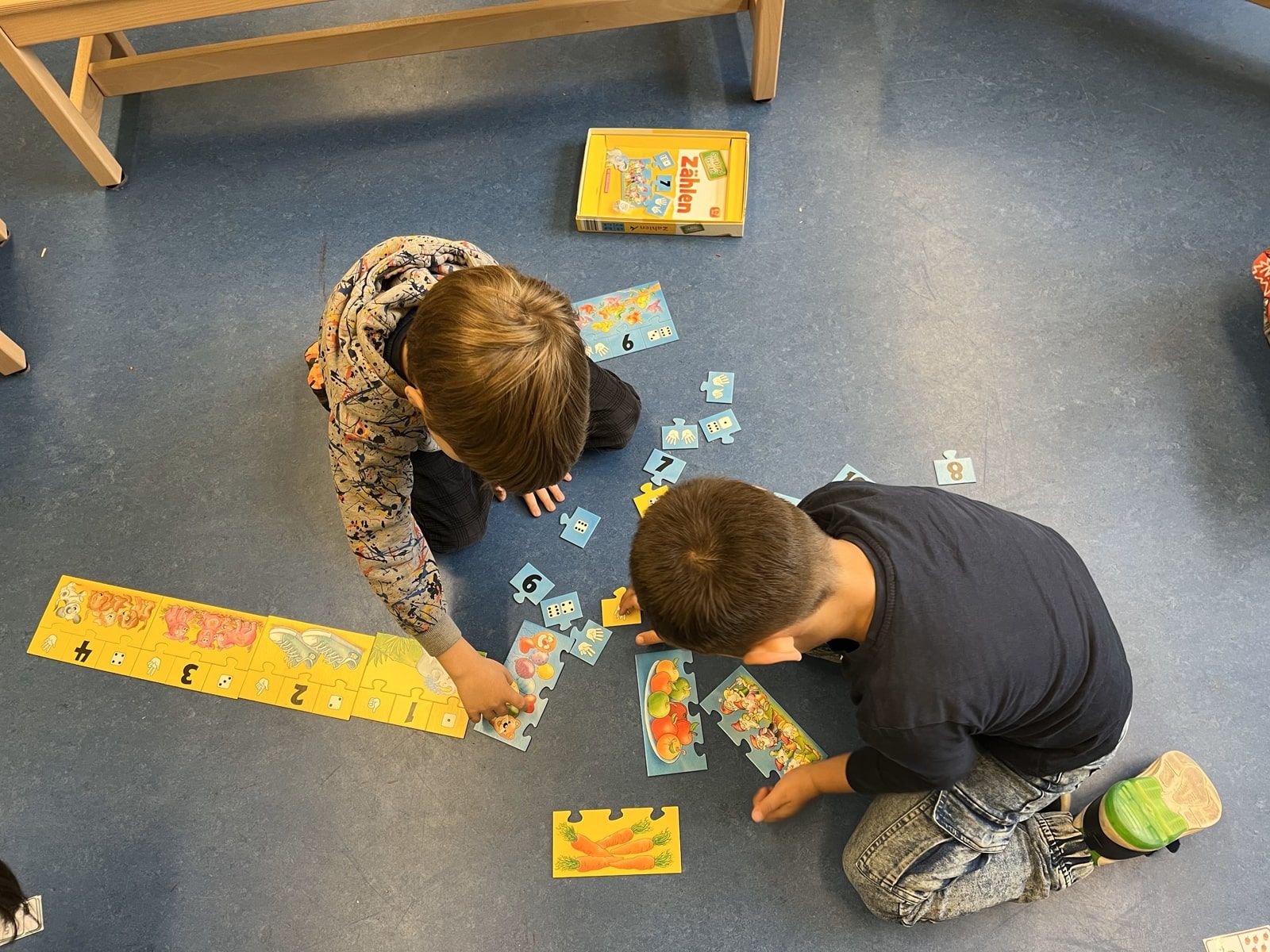 Zwei Kinder spielen mit Zahlenkarten auf dem Boden