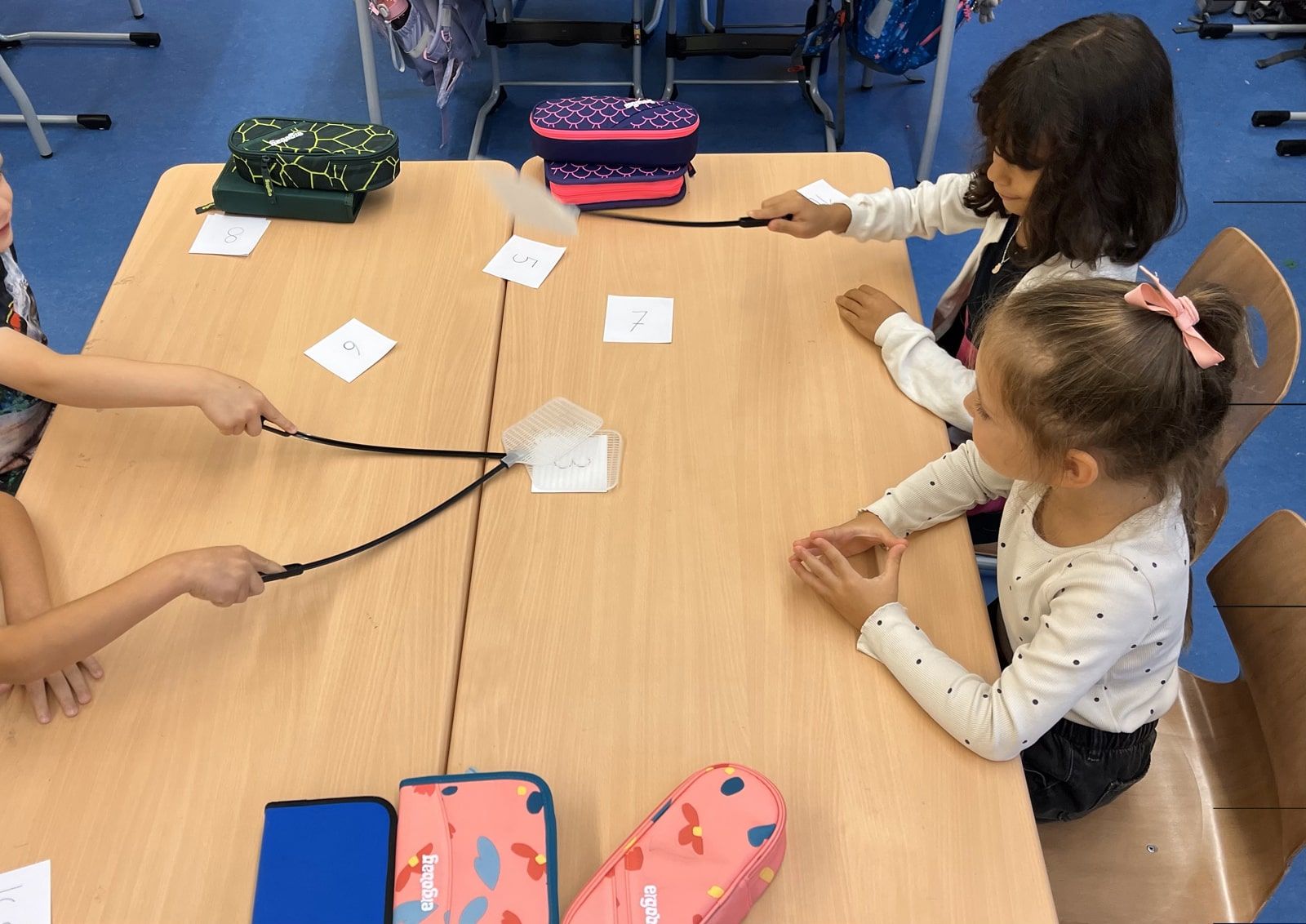 Vier Kinder spielen mit Fliegenklatschen und Zahlenkarten auf dem Tisch