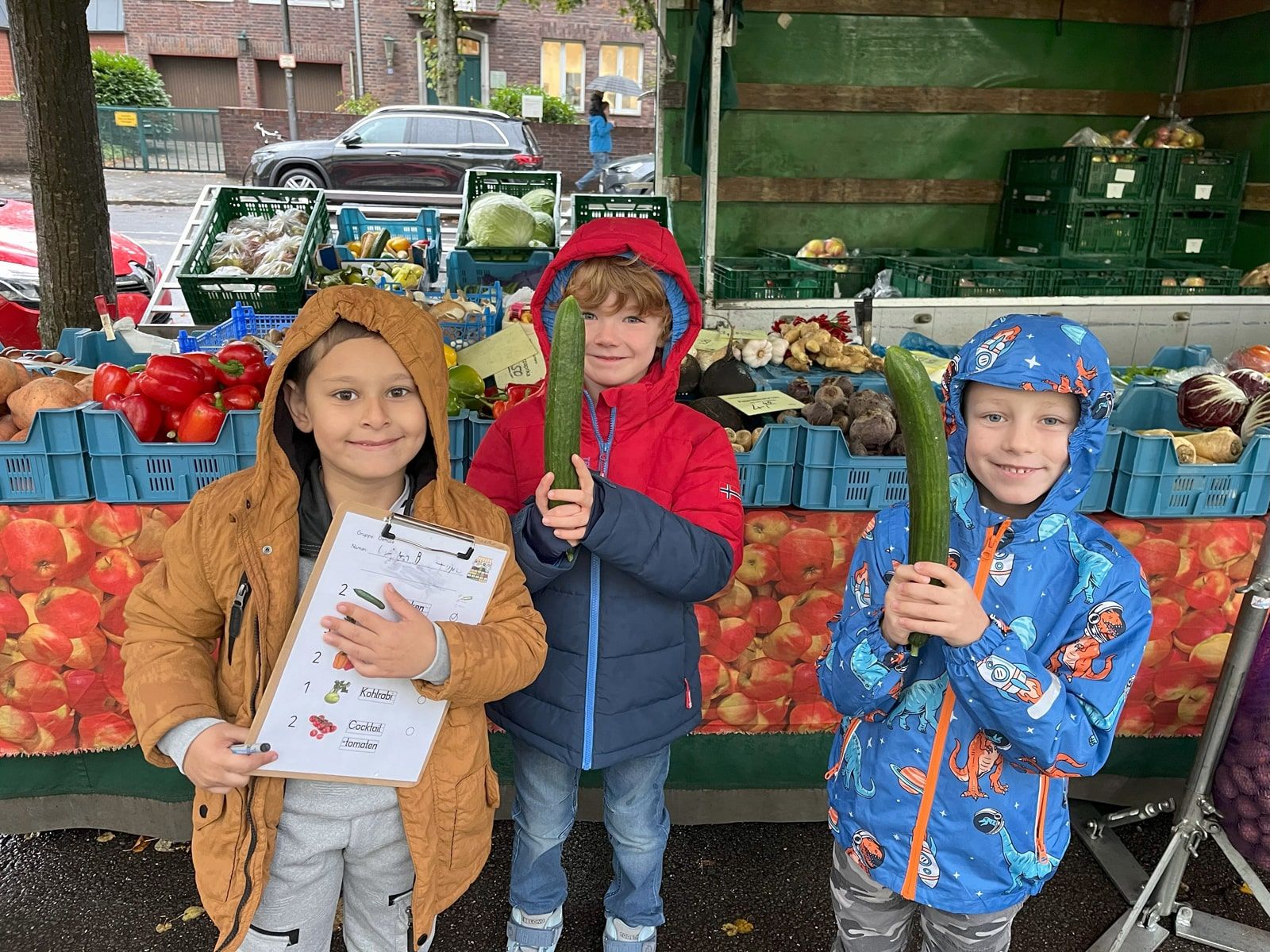 Drei Kinder mit Gurken vor einem Obst- und Gemüse-Stand