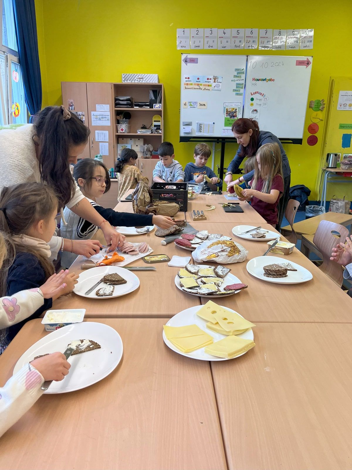 Kinder und Lehrerinnen scheiden Obst und schmieren Brote